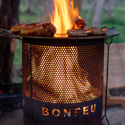 Outdoor grill with flames cooking food, branded 'BONFEU', against a natural background.