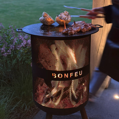 Outdoor grill with 'Bonfeu' branding being used to cook food in a garden setting.