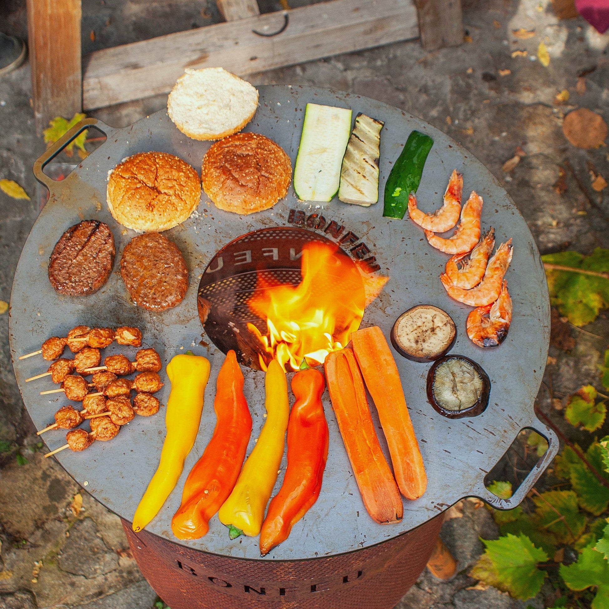 Grill with food items like vegetables and meats over a fire on a stone surface.
