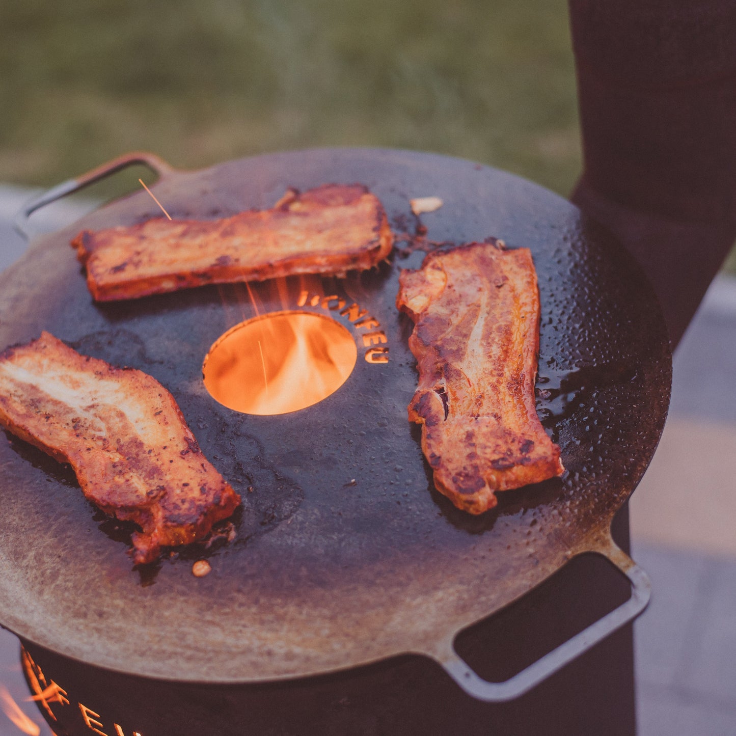 Ribs being cooked on a stone grill over an open flame with a blurred background