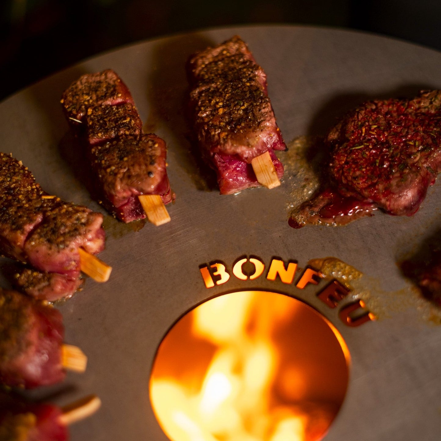 Grilled meat skewers on aBonfeço grill with flames visible.