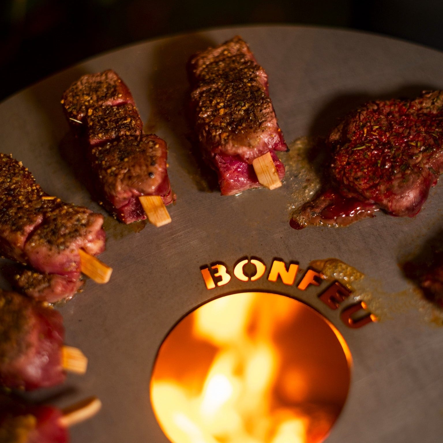 Grilled meat skewers on aBonfeço grill with flames visible.