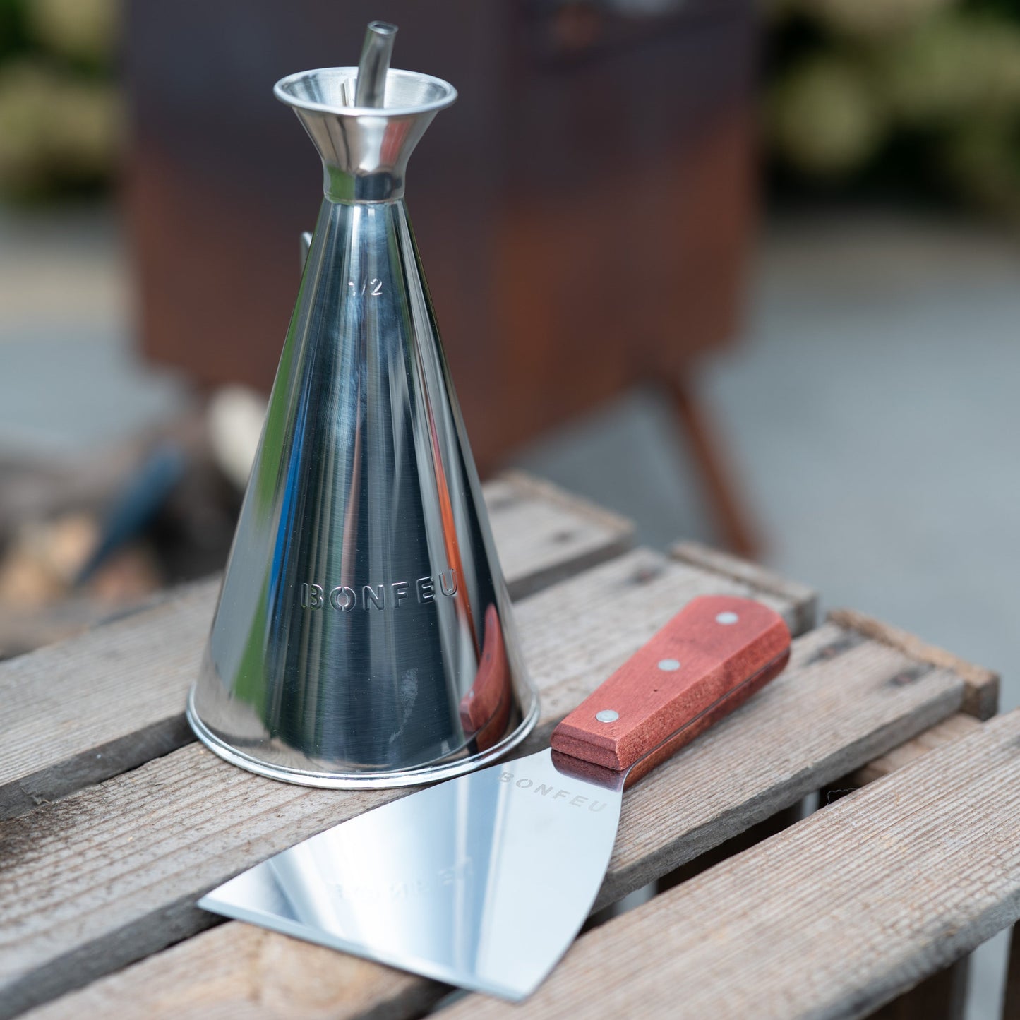 Metal olive oil dispenser and spatula on a wooden surface with a blurred background
