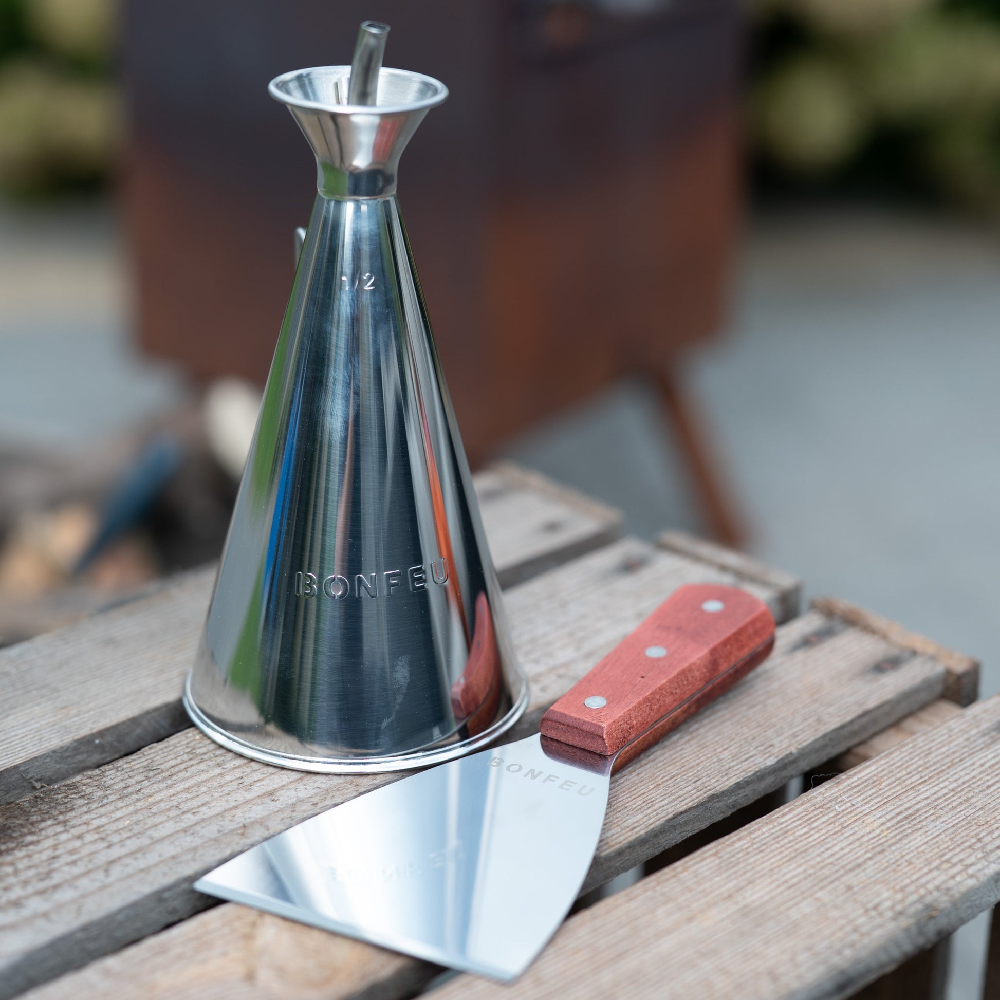 Metal olive oil dispenser and spatula on a wooden surface with a blurred background