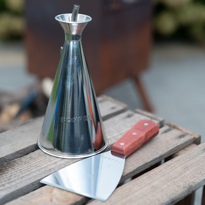 Metal olive oil dispenser and spatula on a wooden surface with a blurred background