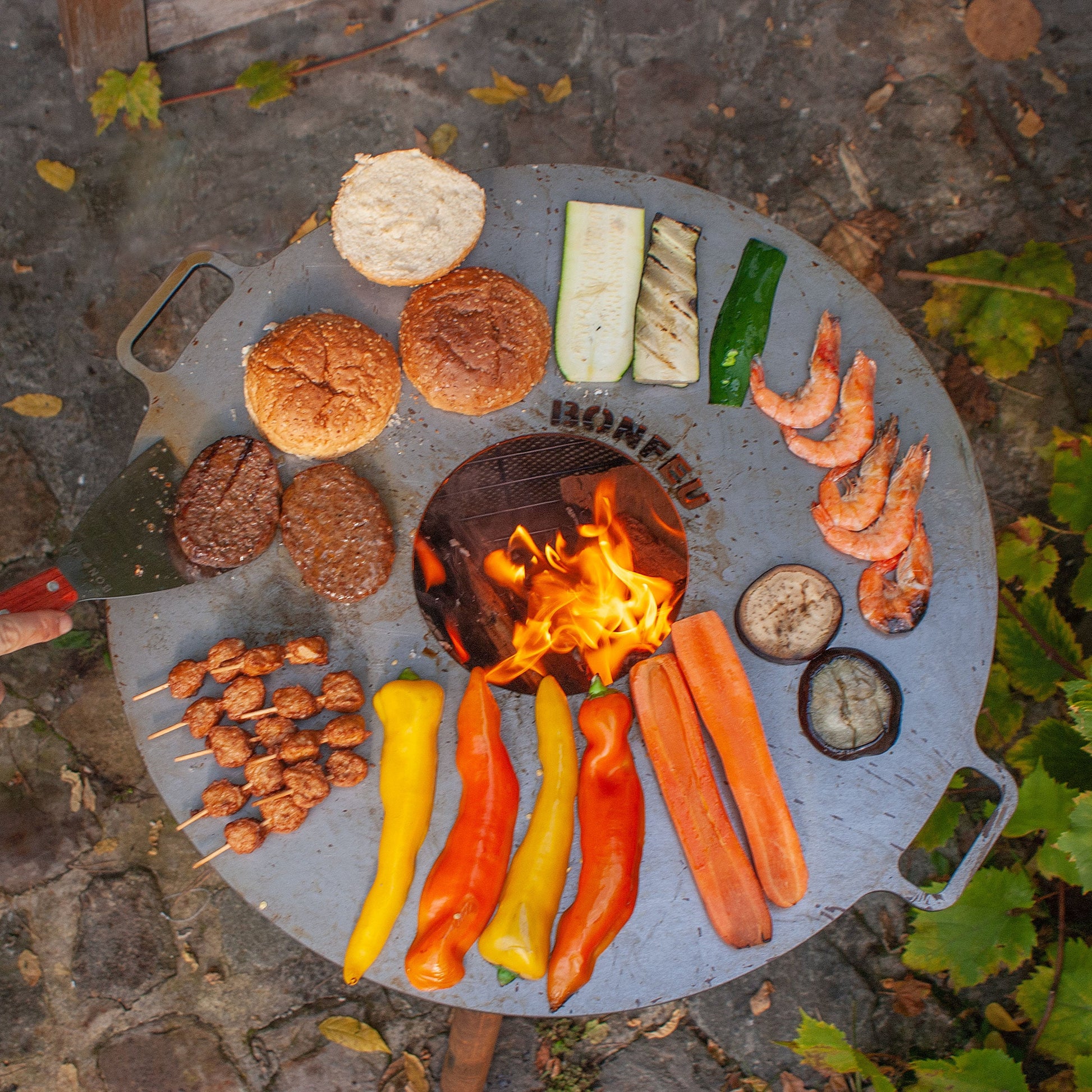 Grill with various food items being cooked over an open flame on a stone surface.